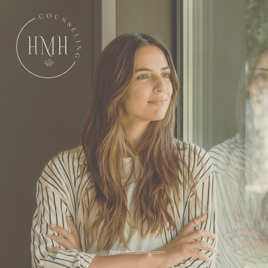Woman gazing out a sunlit window with coffee, quiet moment of reflection: HMH Counseling