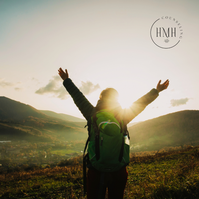 woman with arms overhead triumphantly facing the sun and mountains