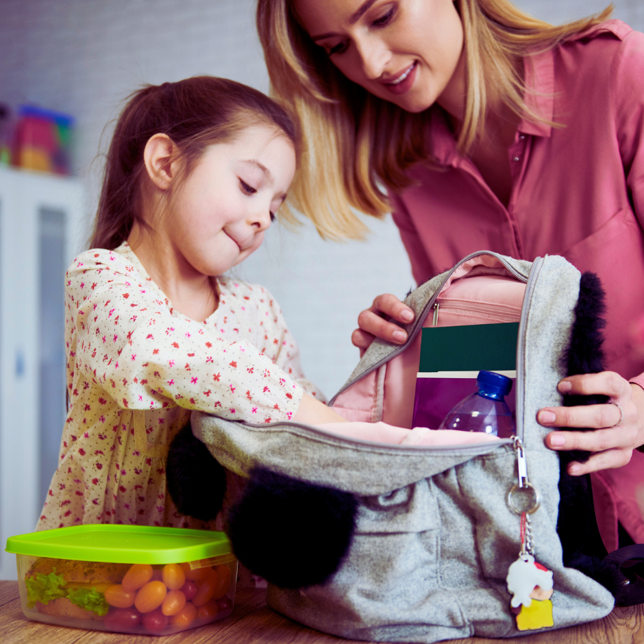 Mother helping young daughter pack book bag