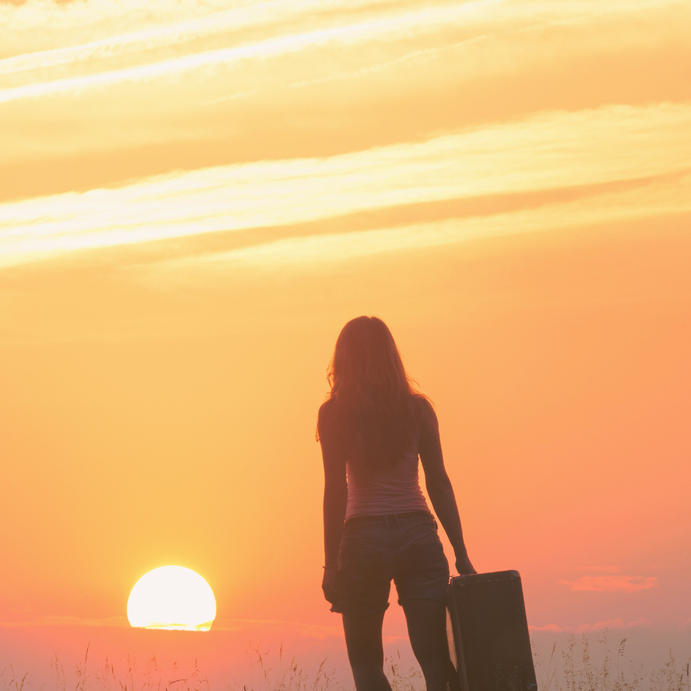 Woman with suite case walking towards the sun