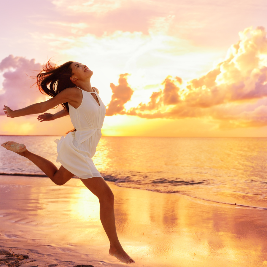 A joyful woman leaping high on a beach, her silhouette framed against a stunningly colorful sky, representing the rejuvenating power of holistic mental health counseling